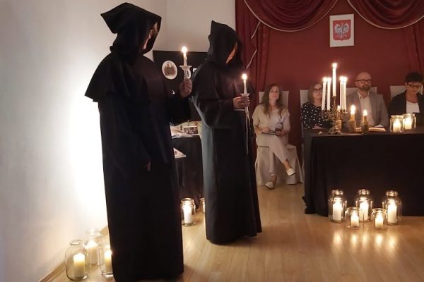 Uczestnik inscenizacji w ciemnym stroju przy stole ze świecami — Narodowe Czytanie w Tucznej, 8 września 2026 r.