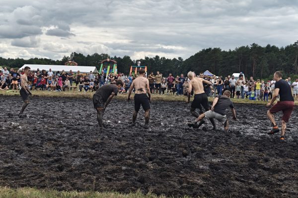 Zawodnicy podczas meczu piłki błotnej na mokrym, błotnistym boisku.
