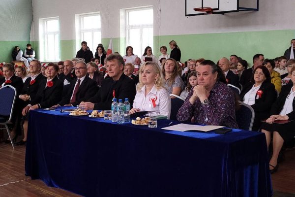 Publiczność i osoby przy stole jury podczas Festiwalu Pieśni Patriotycznych w sali sportowej.