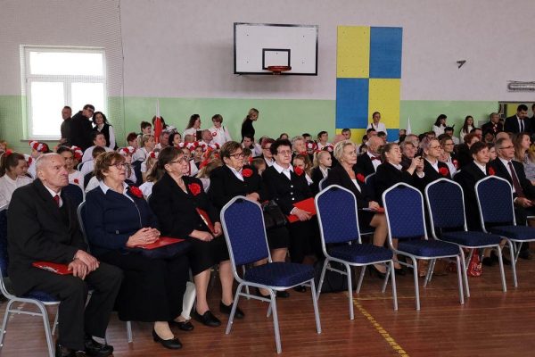 Publiczność i osoby przy stole jury podczas Festiwalu Pieśni Patriotycznych w sali sportowej.