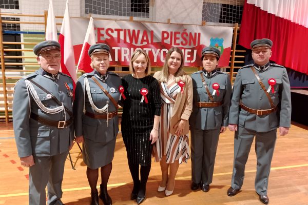 Grupa osób w mundurach i uczestników festiwalu w sali sportowej.