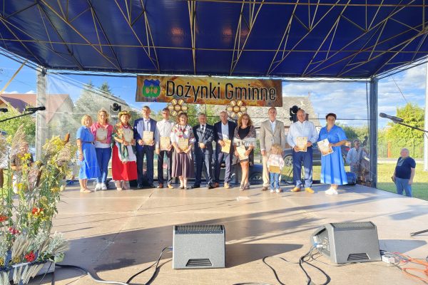 Zespół występujący na scenie ozdobionej wieńcami dożynkowymi.