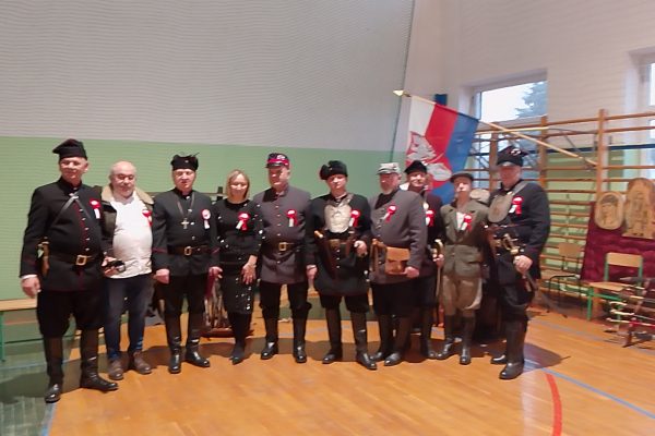 Grupa osób w mundurach i uczestników festiwalu w sali sportowej.