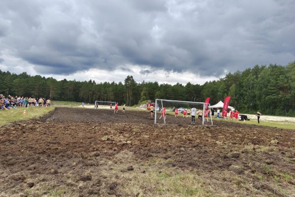 Błotniste boisko piłkarskie z bramkami i wodą.