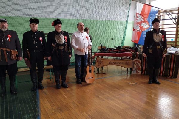Grupa osób w mundurach i uczestników festiwalu w sali sportowej.