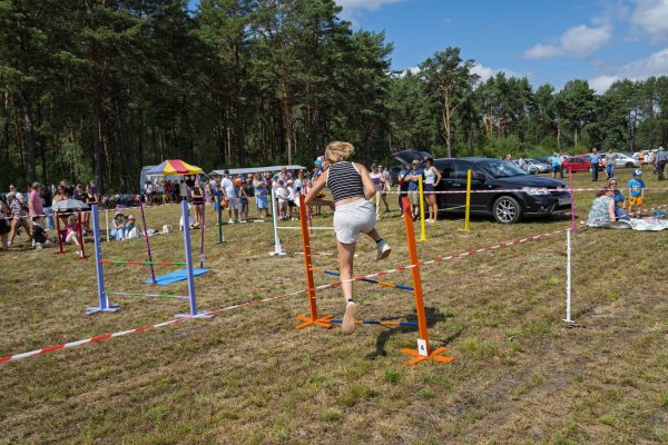 Dzieci pokonujące niskie przeszkody na trawiastym placu wystawy koni.