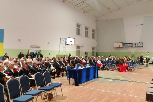 Publiczność i osoby przy stole jury podczas Festiwalu Pieśni Patriotycznych w sali sportowej.