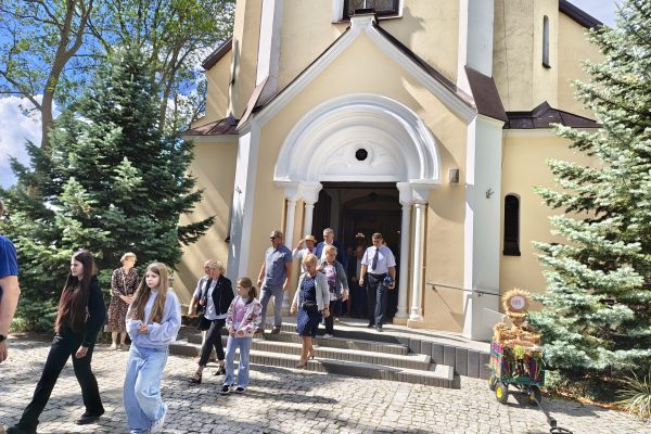 Uczestnicy dożynek z wieńcami i tabliczkami przed kościołem.
