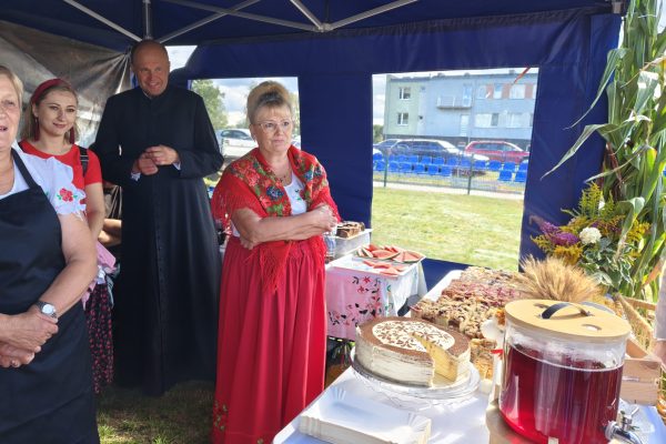 Uczestnicy dożynek przy stoisku z potrawami i dekoracjami z plonów.