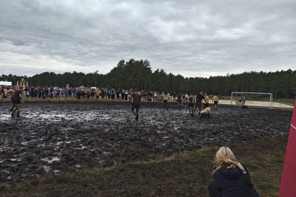 Zawodnicy podczas meczu piłki błotnej na mokrym, błotnistym boisku.