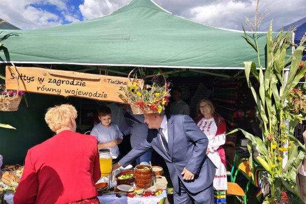 Uczestnicy dożynek przy stoisku z potrawami i dekoracjami z plonów.