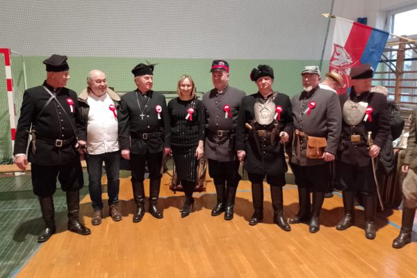 Grupa osób w mundurach i uczestników festiwalu w sali sportowej.