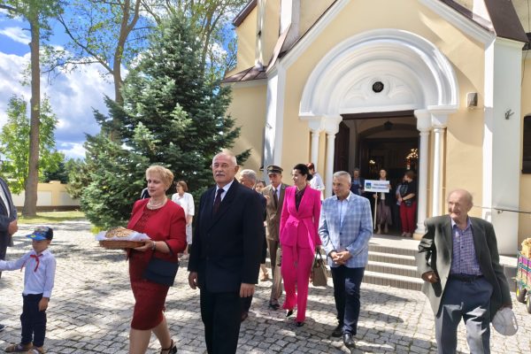 Uczestnicy dożynek z wieńcami i tabliczkami przed kościołem.