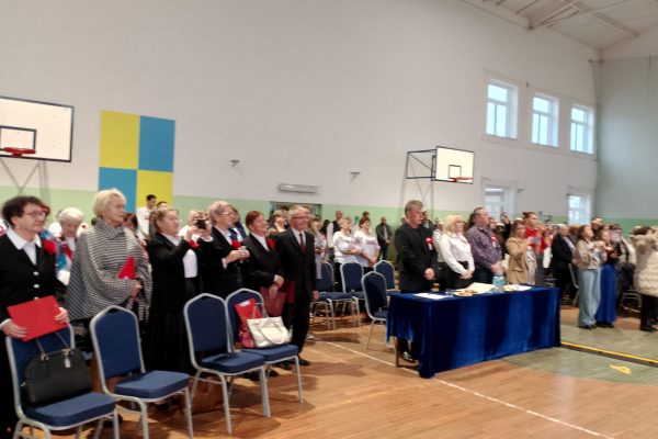 Publiczność i osoby przy stole jury podczas Festiwalu Pieśni Patriotycznych w sali sportowej.