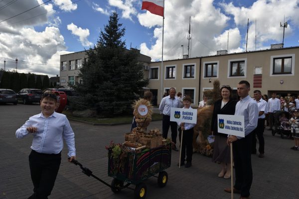 Uczestnicy dożynek z wieńcami i tabliczkami przed kościołem.