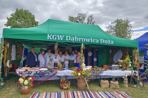 Uczestnicy dożynek przy stoisku z potrawami i dekoracjami z plonów.