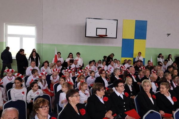 Publiczność i osoby przy stole jury podczas Festiwalu Pieśni Patriotycznych w sali sportowej.