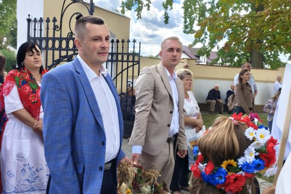 Uczestnicy dożynek z wieńcami i tabliczkami przed kościołem.