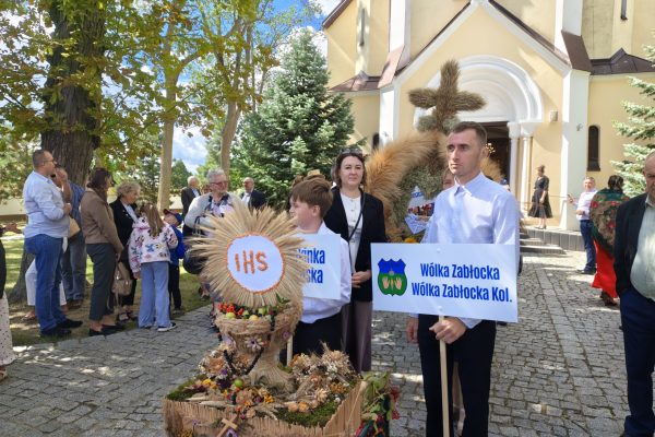 Uczestnicy dożynek z wieńcami i tabliczkami przed kościołem.