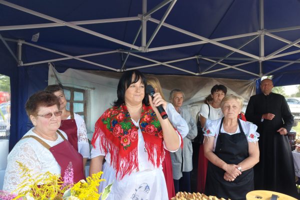Uczestnicy dożynek przy stoisku z potrawami i dekoracjami z plonów.