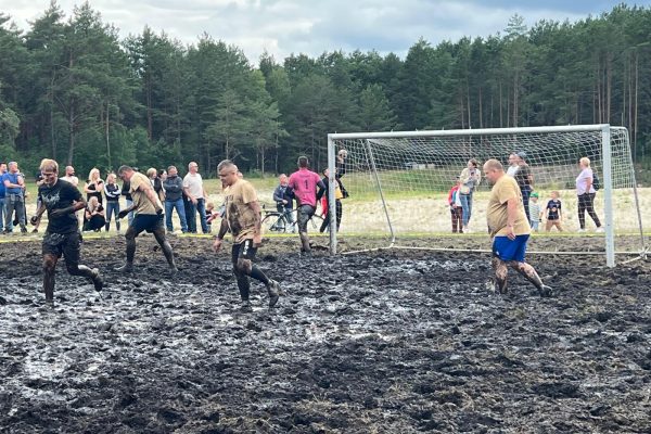 Zawodnicy podczas meczu piłki błotnej na mokrym, błotnistym boisku.