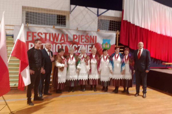 Grupa uczestników festiwalu przy biało-czerwonym banerze.