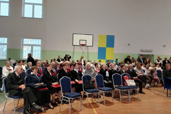 Publiczność i osoby przy stole jury podczas Festiwalu Pieśni Patriotycznych w sali sportowej.
