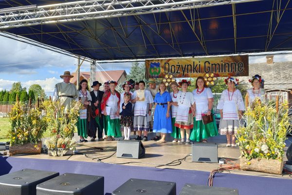 Zespół występujący na scenie ozdobionej wieńcami dożynkowymi.
