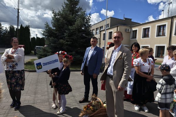 Uczestnicy dożynek z wieńcami i tabliczkami przed kościołem.