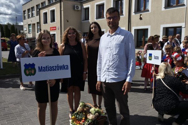 Uczestnicy dożynek z wieńcami i tabliczkami przed kościołem.