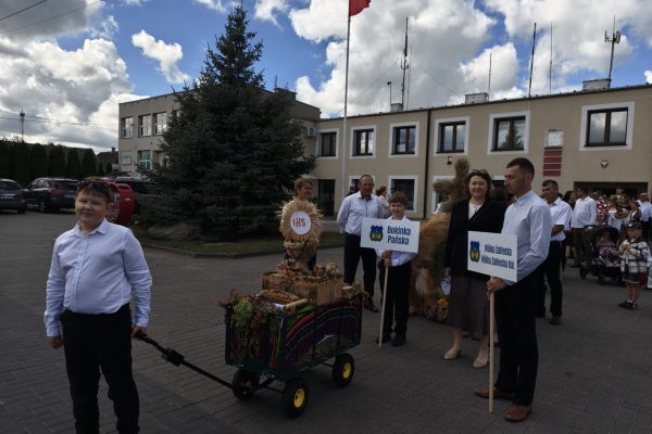 Uczestnicy dożynek z wieńcami i tabliczkami przed kościołem.