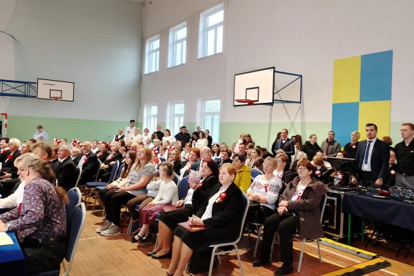 Publiczność i osoby przy stole jury podczas Festiwalu Pieśni Patriotycznych w sali sportowej.