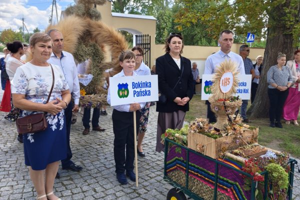 Uczestnicy dożynek z wieńcami i tabliczkami przed kościołem.