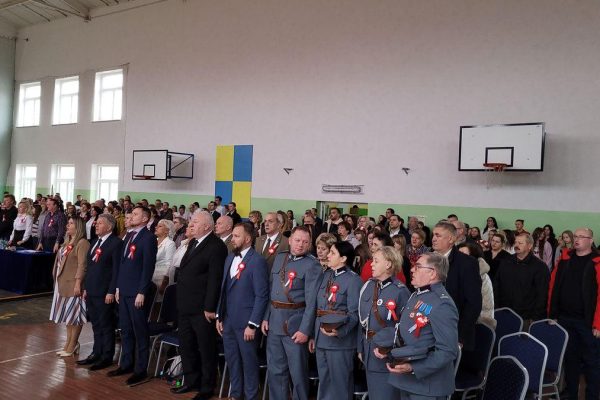 Publiczność i osoby przy stole jury podczas Festiwalu Pieśni Patriotycznych w sali sportowej.