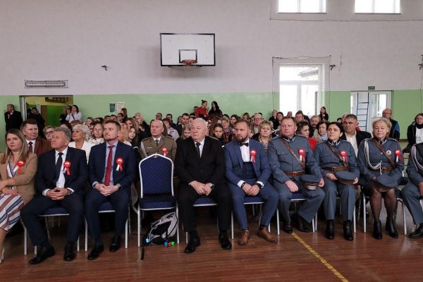 Publiczność i osoby przy stole jury podczas Festiwalu Pieśni Patriotycznych w sali sportowej.