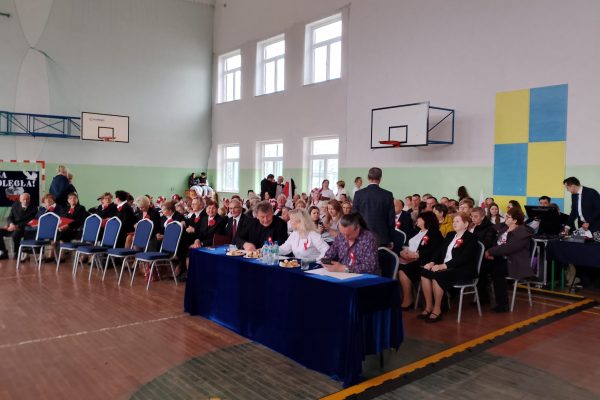 Publiczność i osoby przy stole jury podczas Festiwalu Pieśni Patriotycznych w sali sportowej.