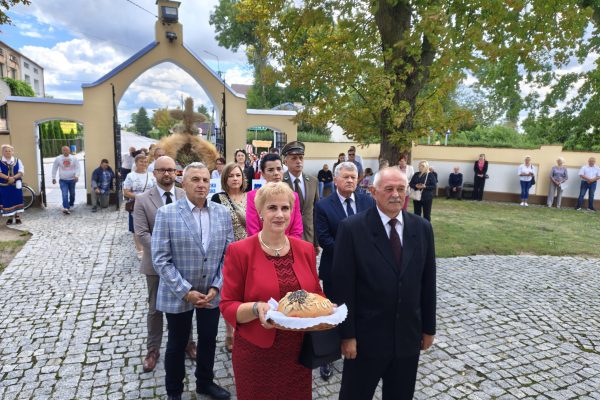 Uczestnicy dożynek z wieńcami i tabliczkami przed kościołem.