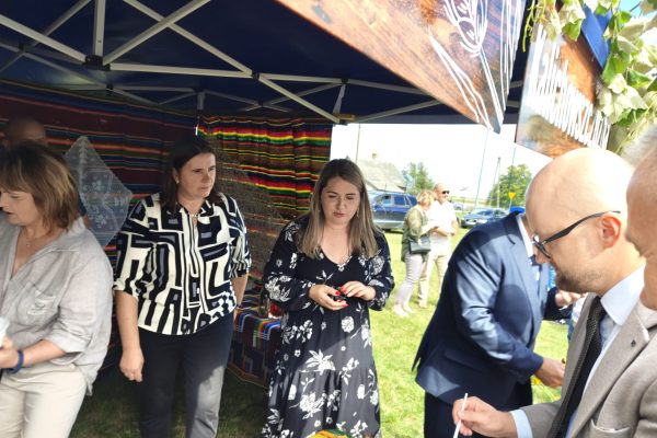 Uczestnicy dożynek przy stoisku z potrawami i dekoracjami z plonów.