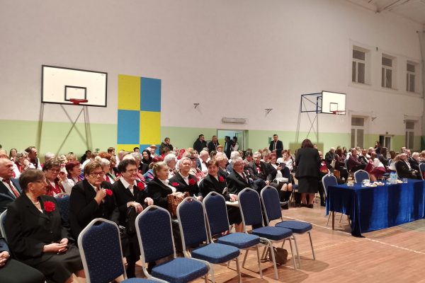 Publiczność i osoby przy stole jury podczas Festiwalu Pieśni Patriotycznych w sali sportowej.