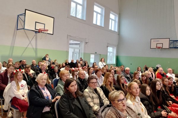 Publiczność i osoby przy stole jury podczas Festiwalu Pieśni Patriotycznych w sali sportowej.